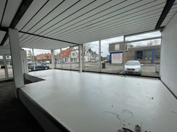 Leegstaand winkelpand aan de Ophelialaan met grote raampartijen en uitzicht op straat en geparkeerde auto's.