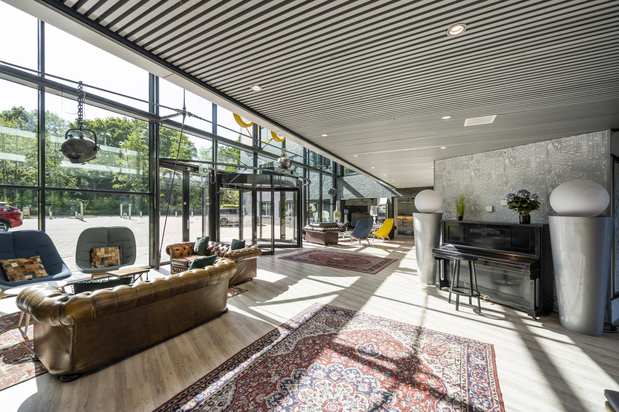 Moderne en lichte lobby aan de Prof. W.H. Keesomlaan met zithoeken, een piano en grote raampartijen.