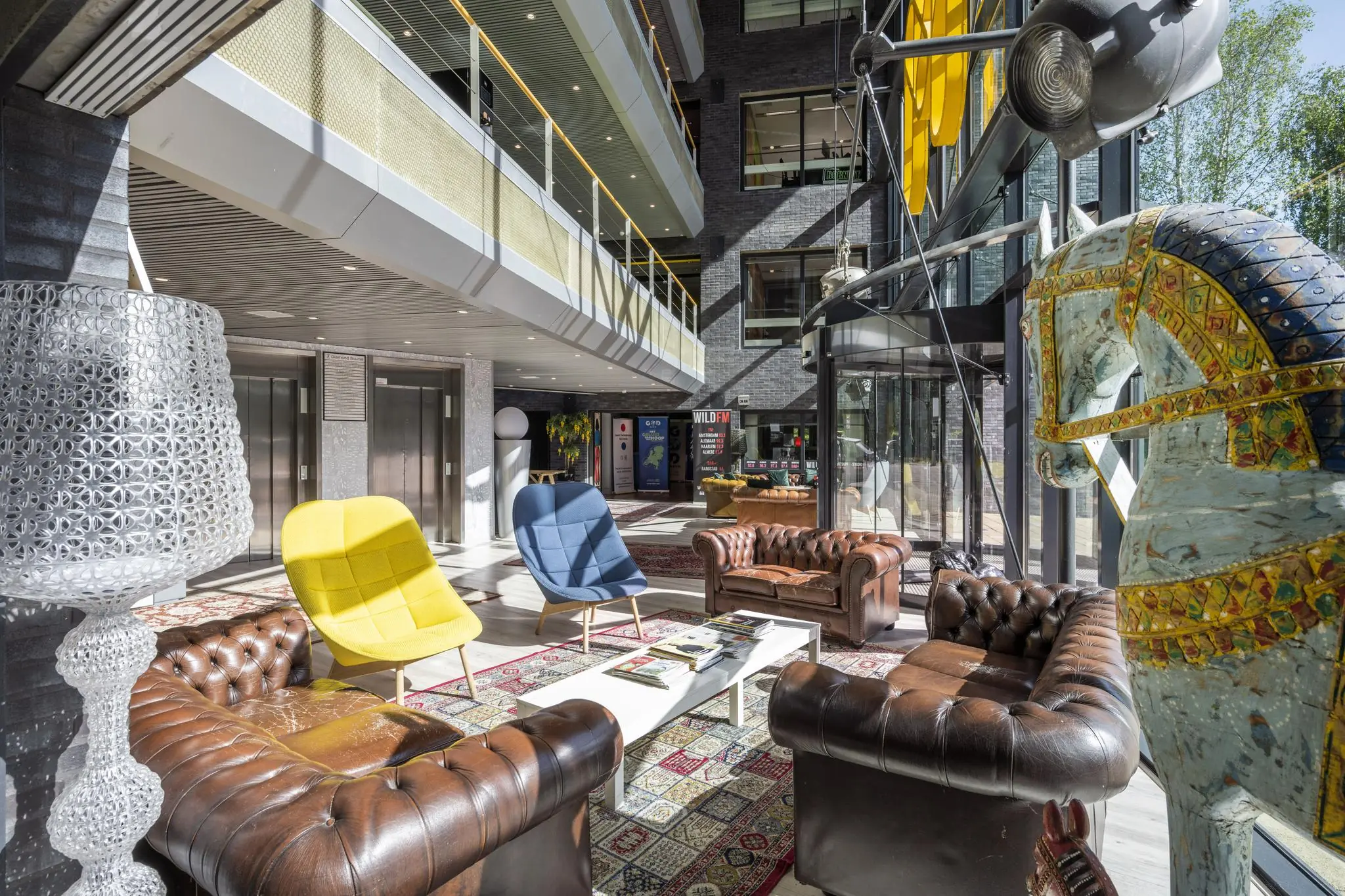 Moderne kantoorlobby aan de Prof. W.H. Keesomlaan met vintage meubilair, kleurrijke stoelen en decoratief houten paard.