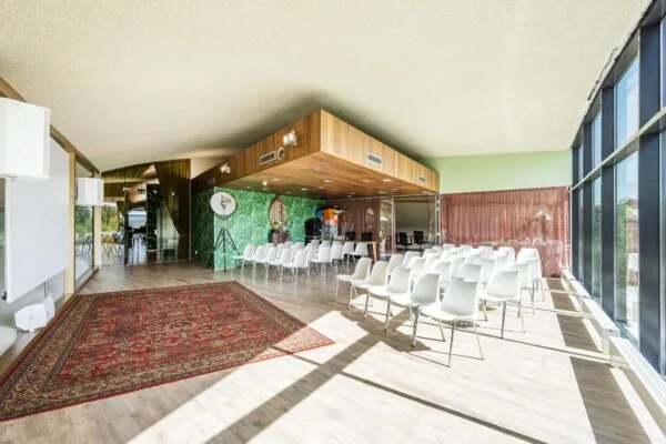 Lichte, moderne conferentieruimte aan de Prof. W.H. Keesomlaan met rijen witte stoelen, groot raam en decoratieve elementen.