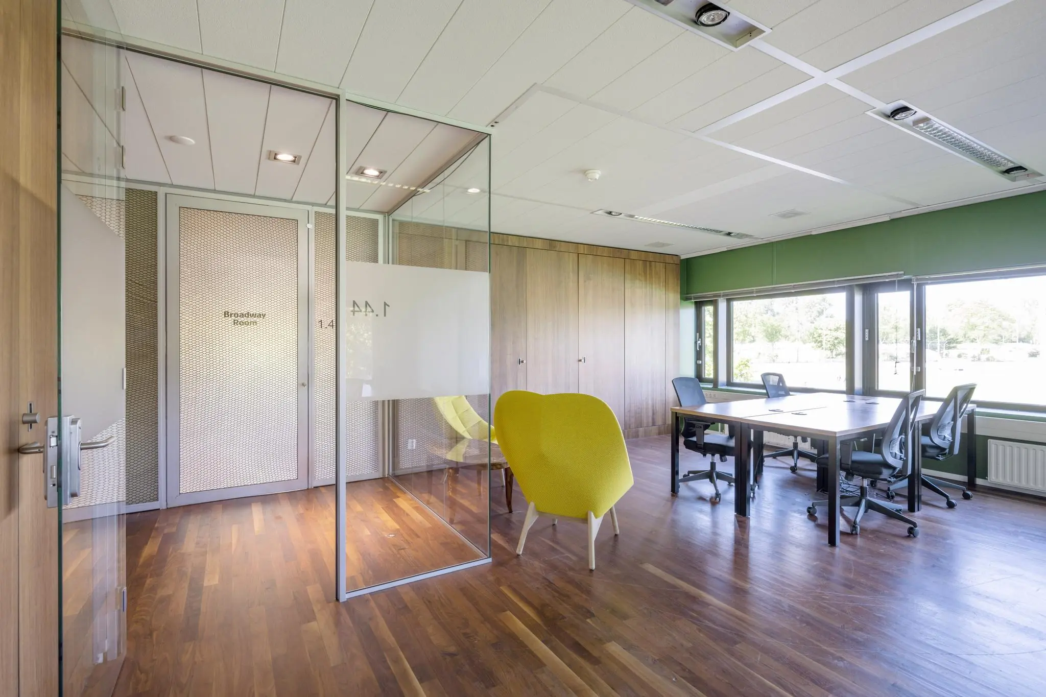 Moderne vergaderruimte aan de Prof. W.H. Keesomlaan met glazen wanden, houten vloer, werkplekken en een opvallende gele stoel.