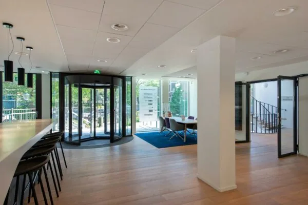 Moderne entreehal van een kantoor aan de Bezuidenhoutseweg met houten vloer, draaideur en vergaderruimte.