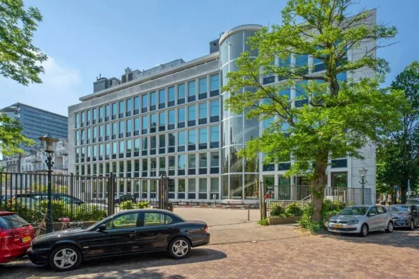 Modern kantoorgebouw aan de Bezuidenhoutseweg in Den Haag met glazen gevel en geparkeerde auto's op de voorgrond.