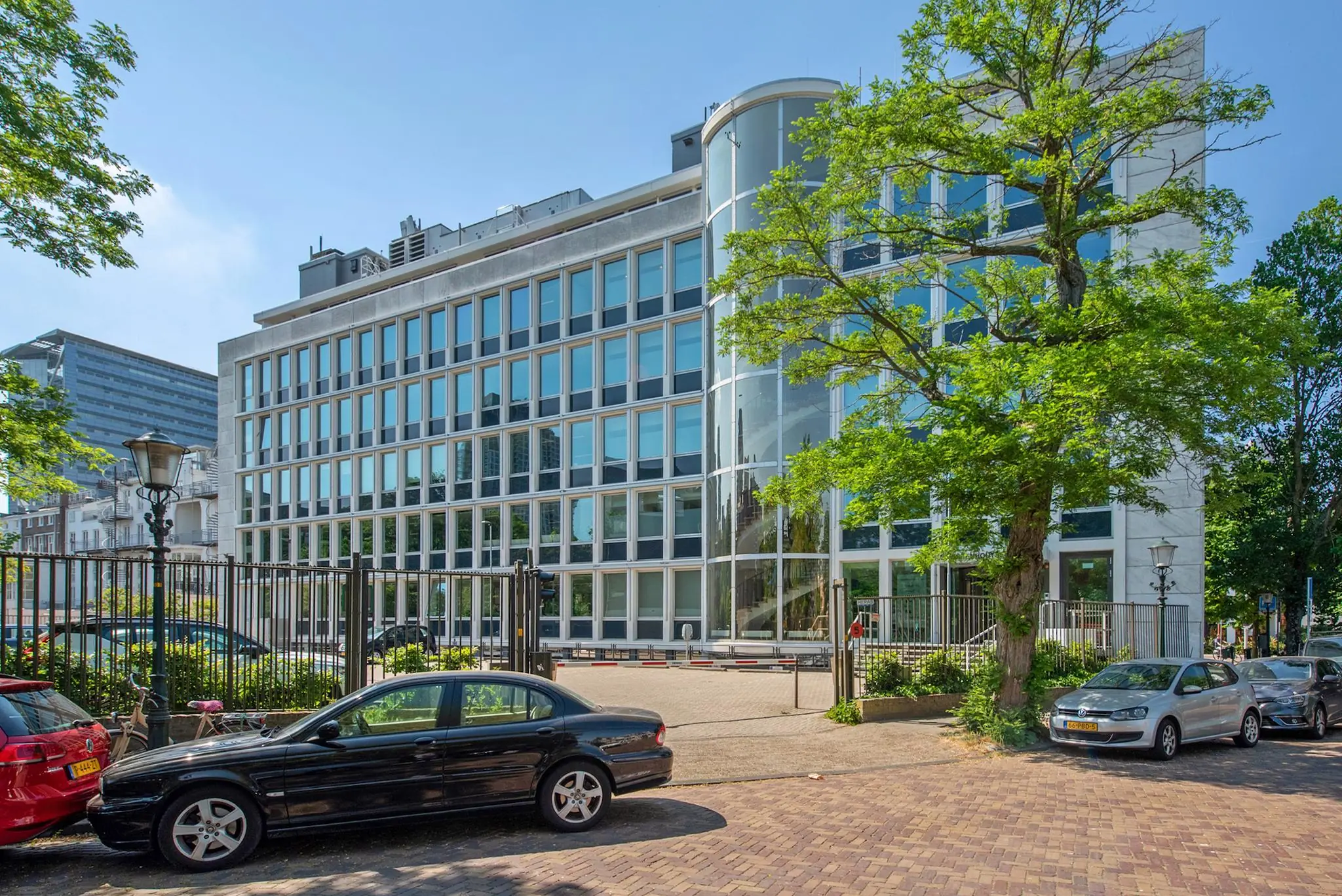 Modern kantoorgebouw aan de Bezuidenhoutseweg in Den Haag met glazen gevel en geparkeerde auto's op de voorgrond.