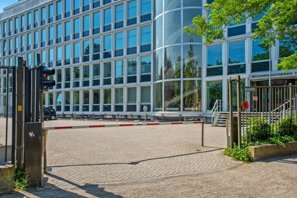 Ingang van een modern kantoorpand aan de Bezuidenhoutseweg met slagboom en glazen trappenhuis.