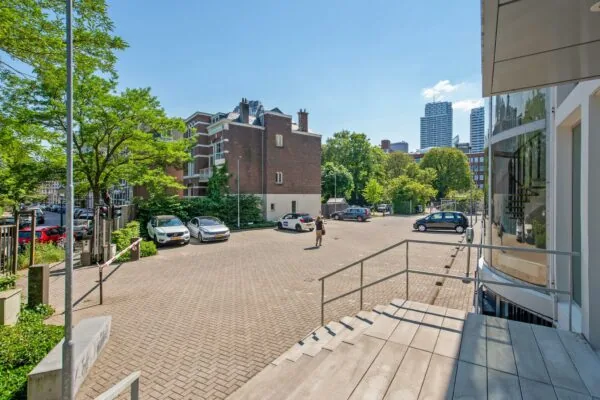Parkeerterrein aan de Bezuidenhoutseweg in Den Haag met geparkeerde auto’s, een voetganger en uitzicht op moderne kantoorgebouwen.