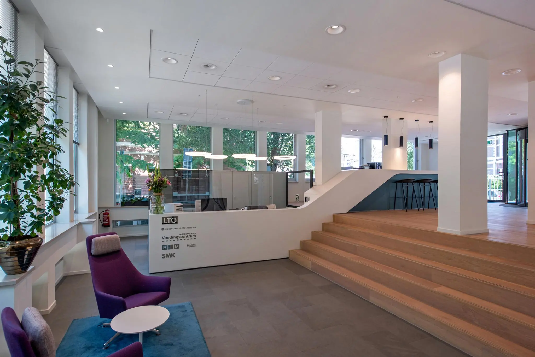 Moderne ontvangstruimte aan de Bezuidenhoutseweg met receptiebalie, zitgedeelte en trap naar verhoogde werkruimte.