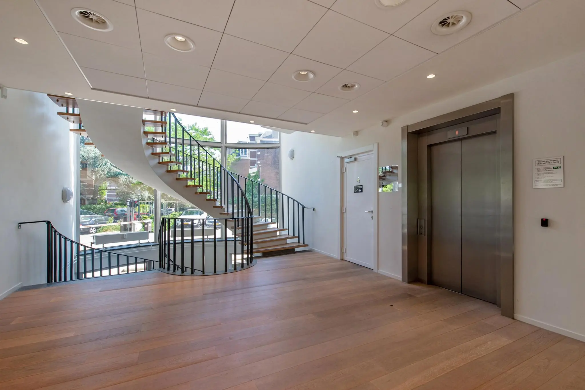 Moderne entreehal aan de Bezuidenhoutseweg met houten vloer, stalen wenteltrap en lift.