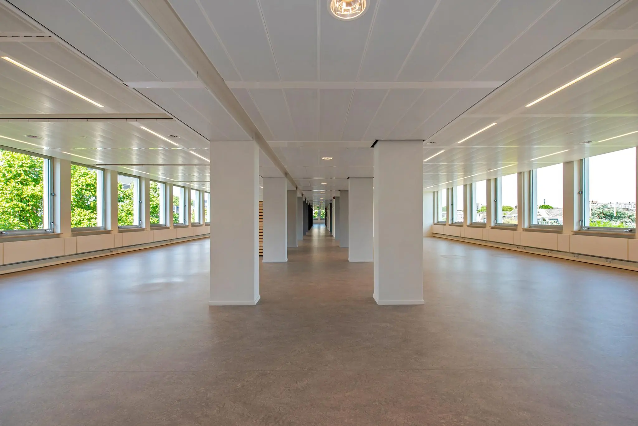 Lichte, lege kantoorruimte met witte pilaren en grote ramen aan de Bezuidenhoutseweg.