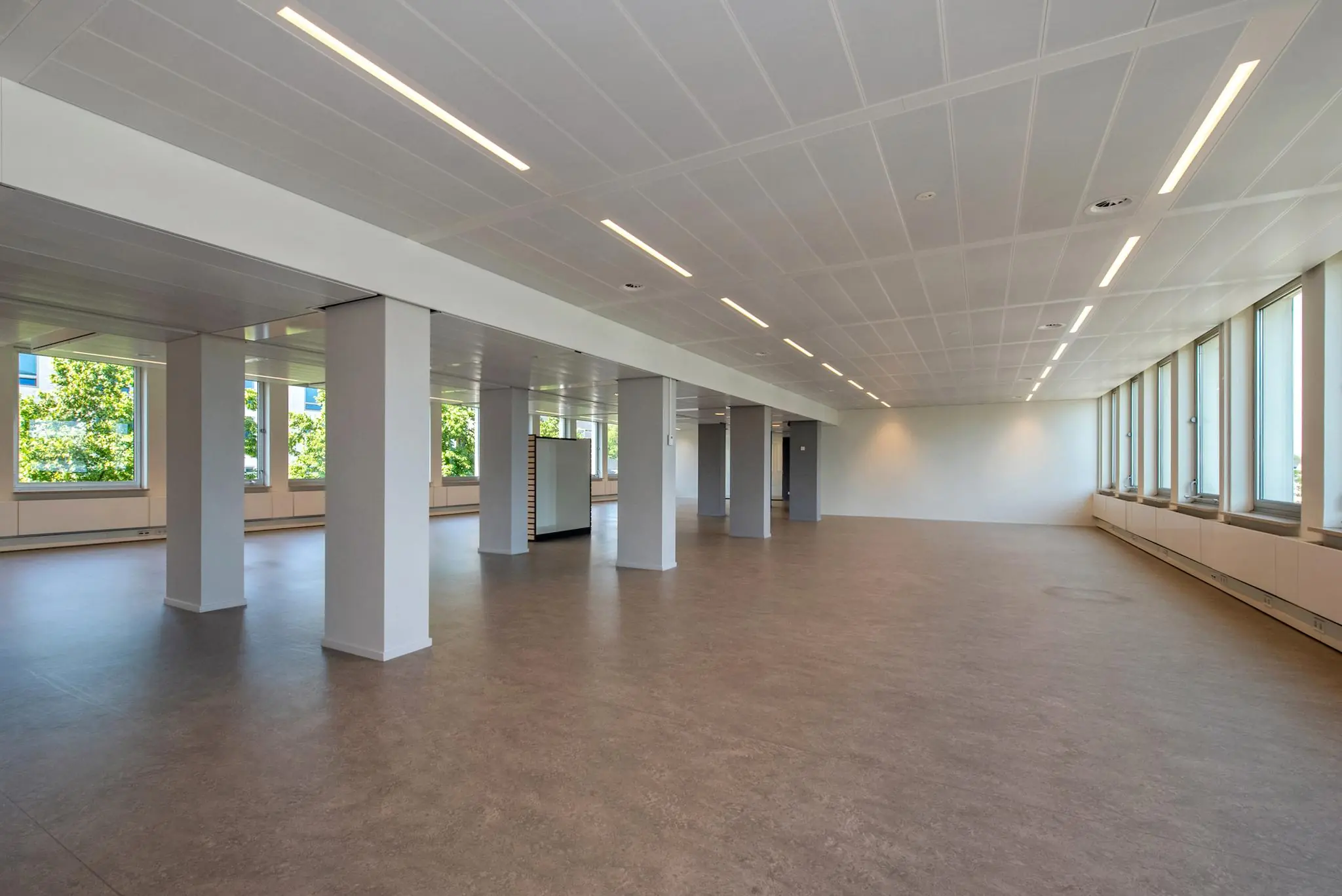 Leeg kantoorpand aan de Bezuidenhoutseweg met grote ramen, kolommen en een systeemplafond.
