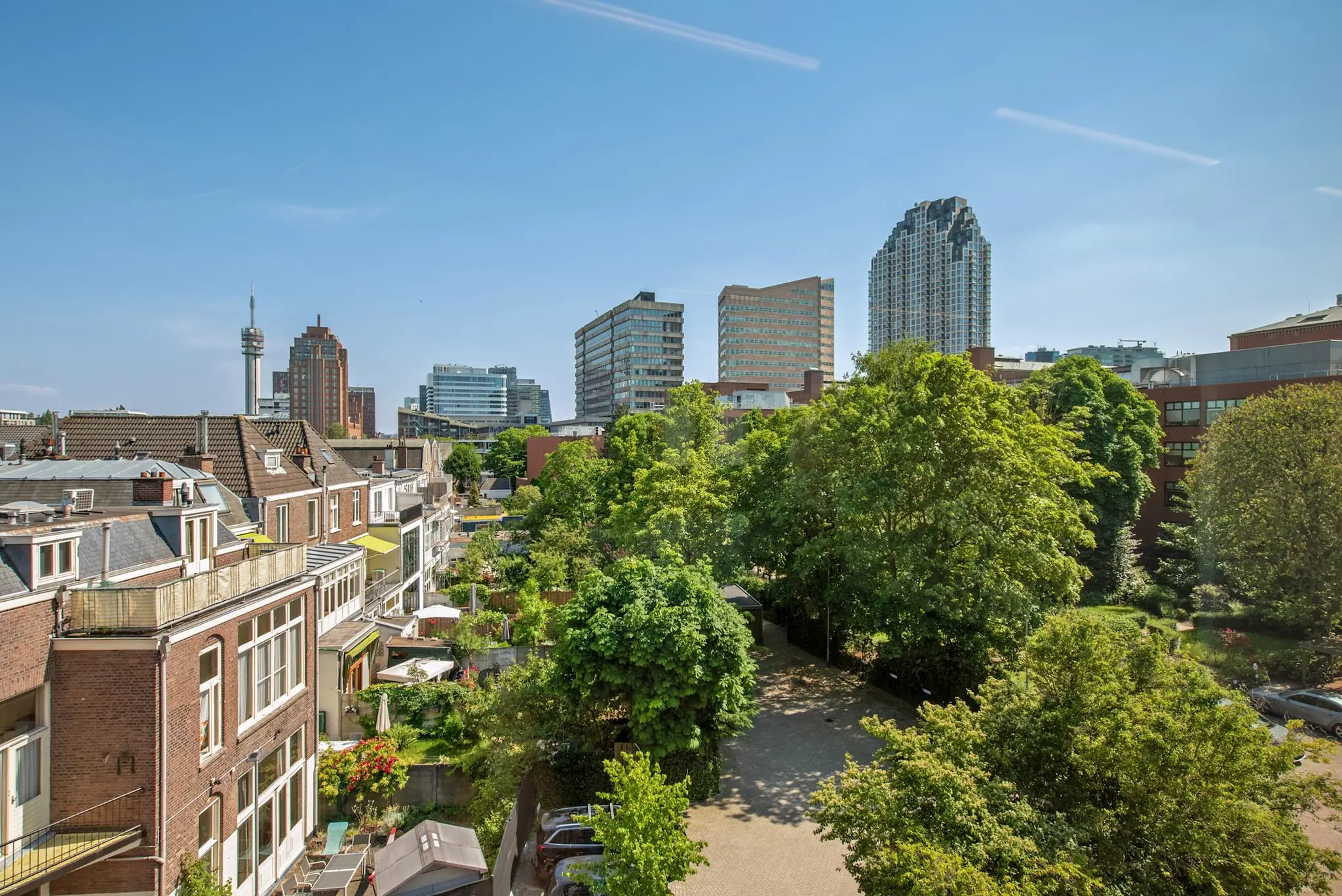 Uitzicht op de Bezuidenhoutseweg in Den Haag met een mix van oude woningen, moderne hoogbouw en veel groen op een zonnige dag.