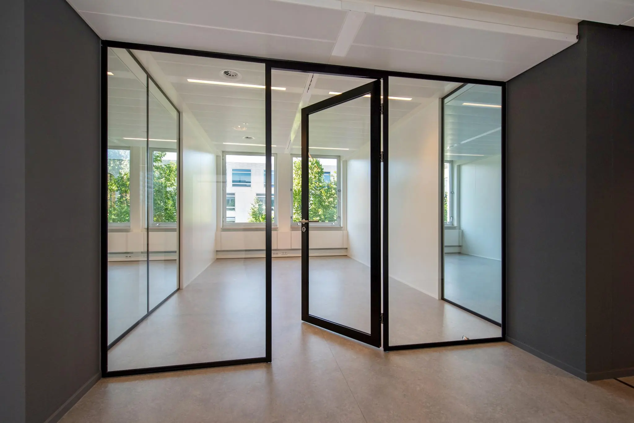 Moderne, lichte kantoorruimte aan de Bezuidenhoutseweg met glazen wanden en een openstaande deur.