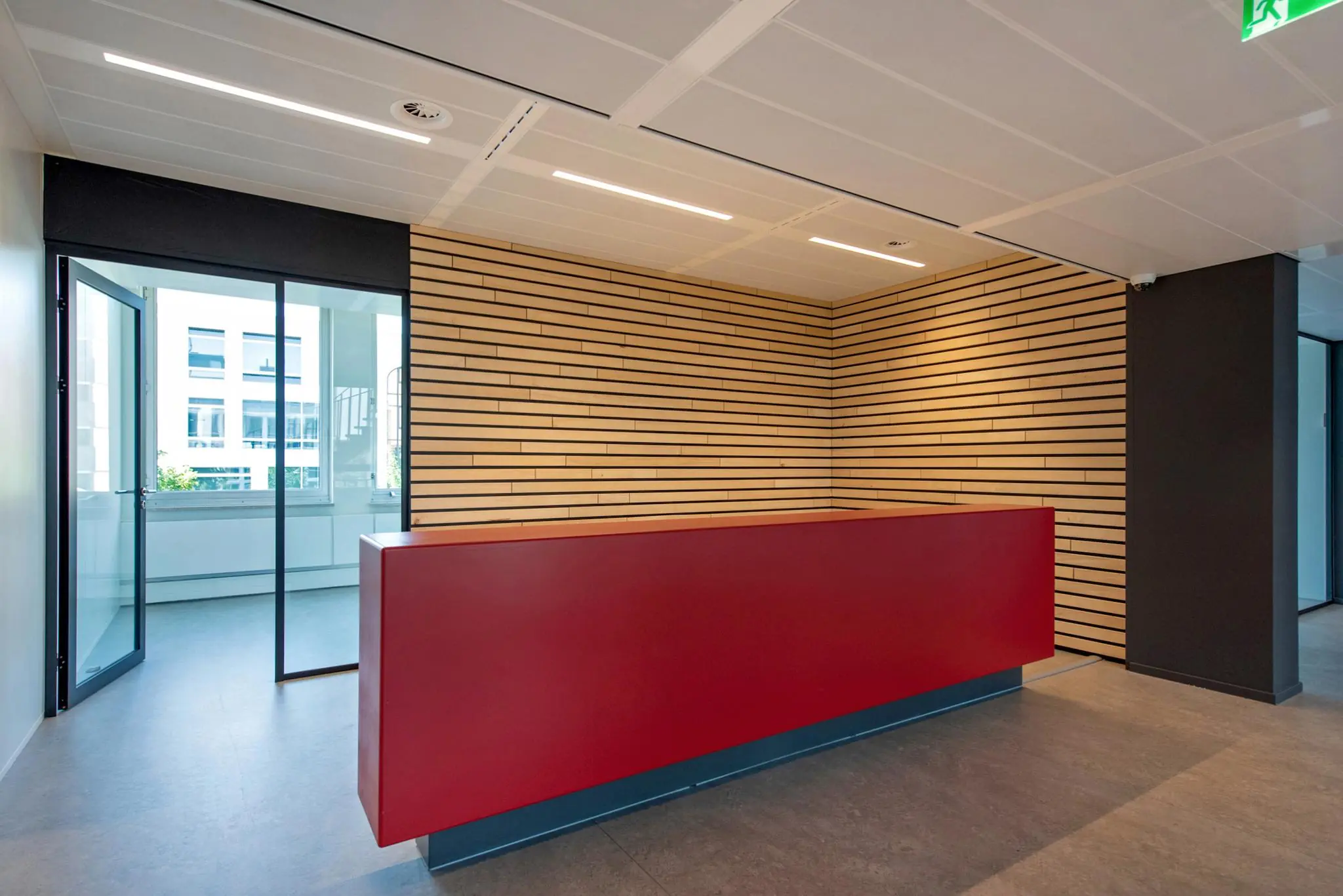 Moderne receptiebalie met rode voorzijde in een strak kantoorinterieur aan de Bezuidenhoutseweg.