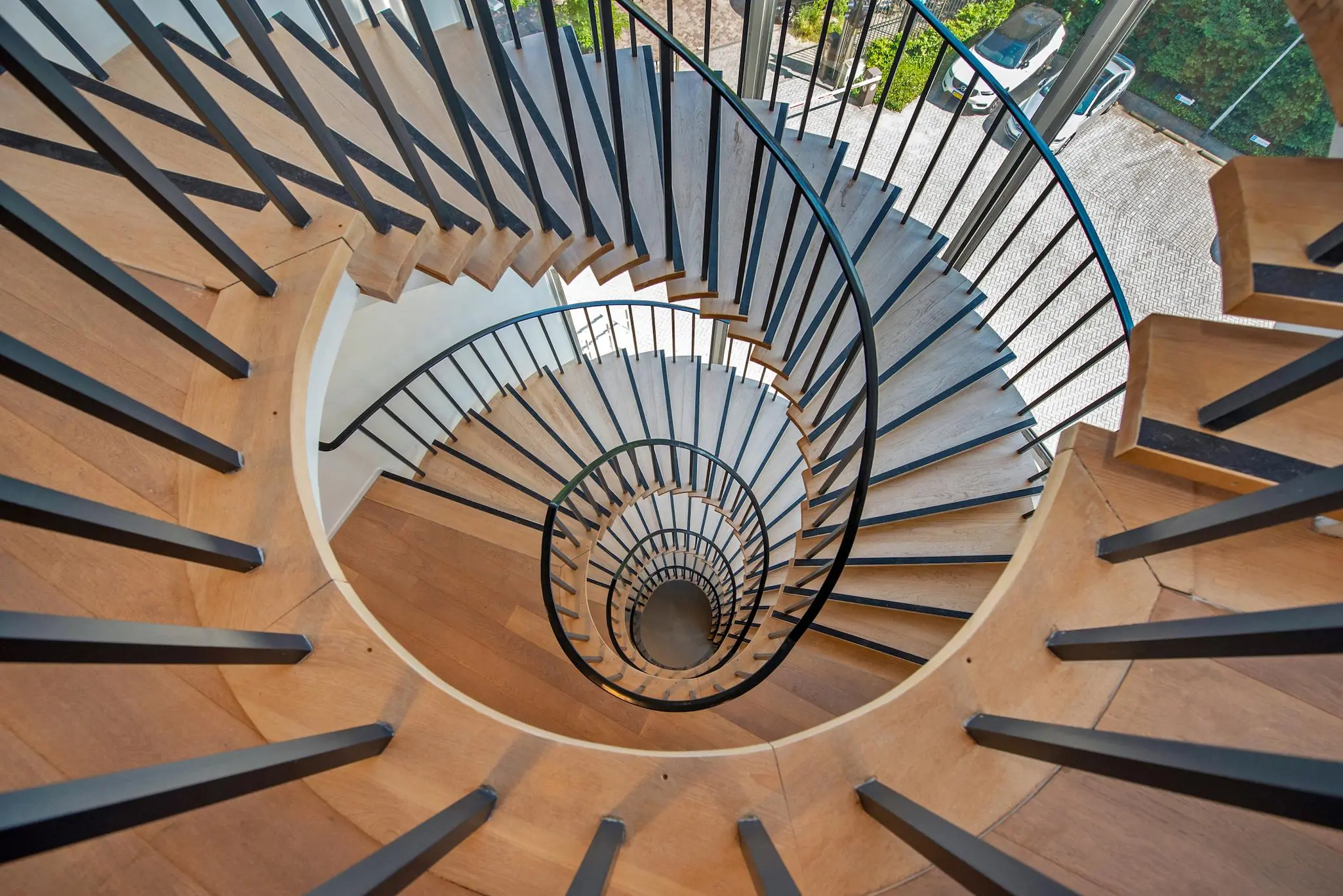 Houten wenteltrap met zwarte leuning in een modern gebouw aan de Bezuidenhoutseweg.