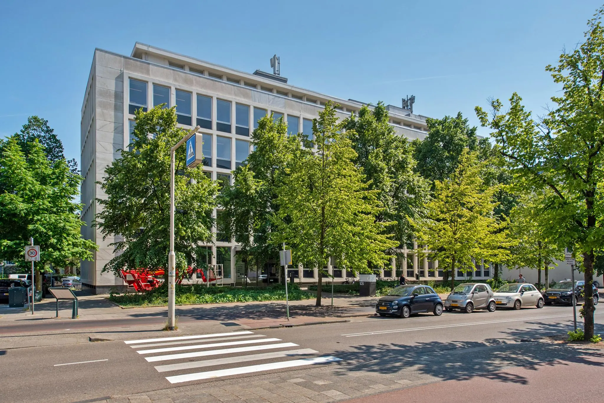 Kantoorgebouw aan de Bezuidenhoutseweg in Den Haag met bomen en geparkeerde auto's op de voorgrond.