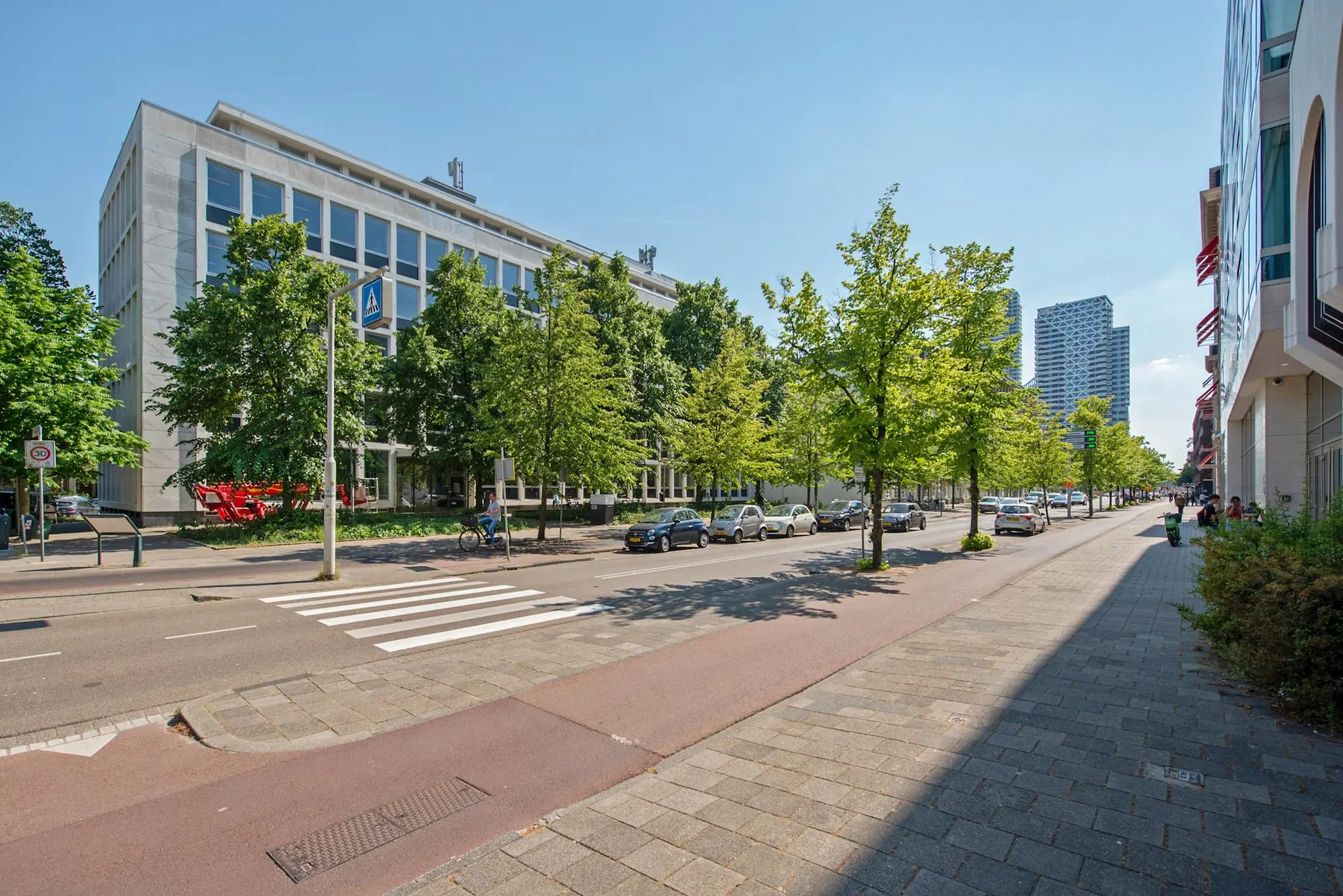 Straatbeeld van de Bezuidenhoutseweg in Den Haag met kantoorpanden, geparkeerde auto's en moderne hoogbouw in de verte.