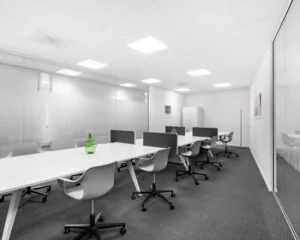 Moderne, minimalistische kantoorruimte met witte bureaus, grijze stoelen en groene decoratieve vazen.