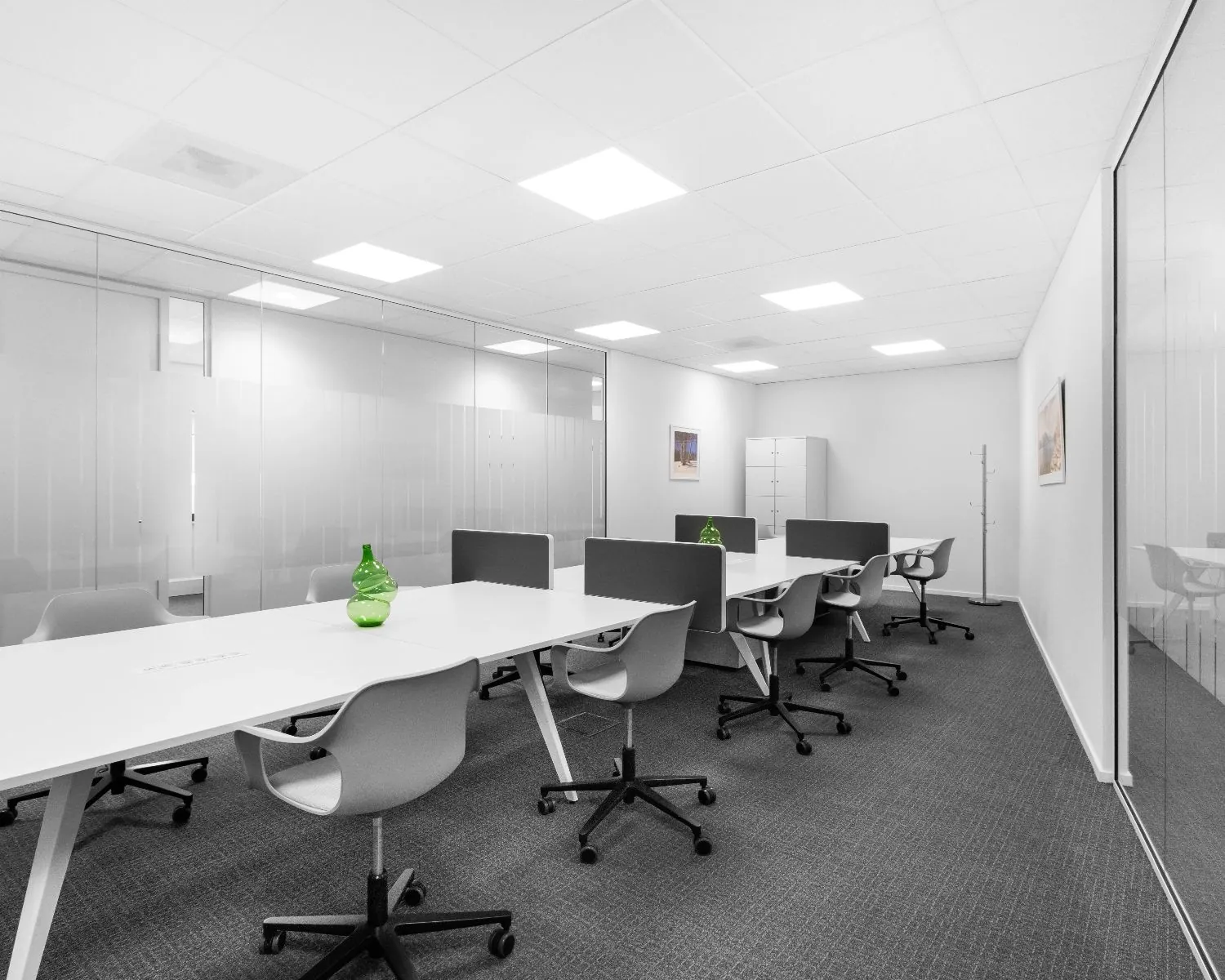 Moderne, minimalistische kantoorruimte met witte bureaus, grijze stoelen en groene decoratieve vazen.