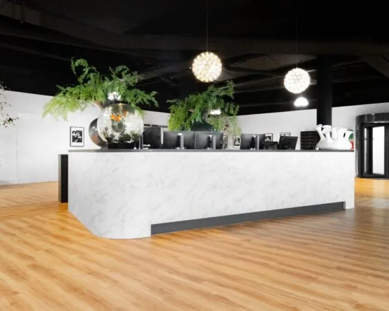 Moderne receptiebalie met marmerlook, computerschermen en grote glazen vazen met planten en goudvissen.