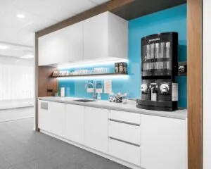 Moderne kantoorkeuken met witte kasten, een Nespresso koffieautomaat en een felblauwe achterwand.
