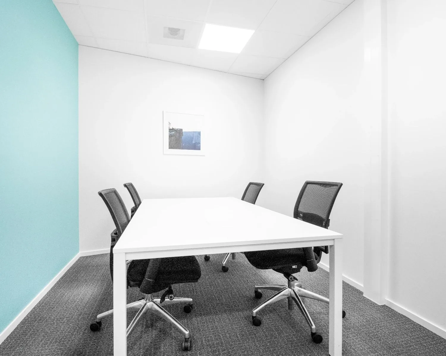 Kleine vergaderruimte met een witte tafel, vier bureaustoelen en een turquoise muur.