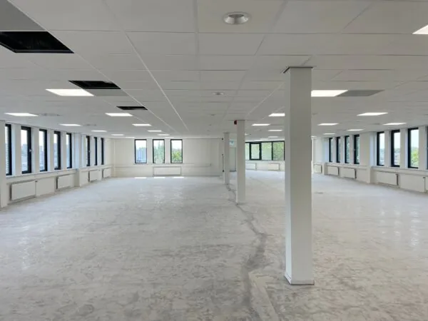 Leeg kantoorpand aan de Vlierbaan met grote ramen, witte wanden en systeemplafond.