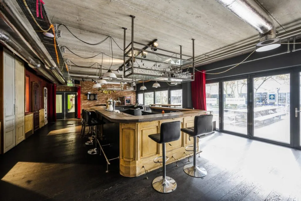 Industrieel ingerichte horecaruimte met houten bar, barkrukken en grote ramen bij Diemermere.