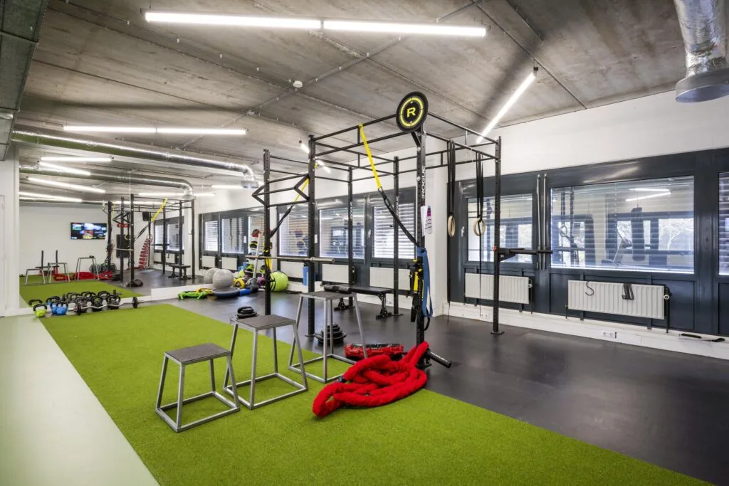 Een moderne fitnessruimte in Diemermere met diverse trainingsapparaten, gewichten en een kunstgrasvloer.