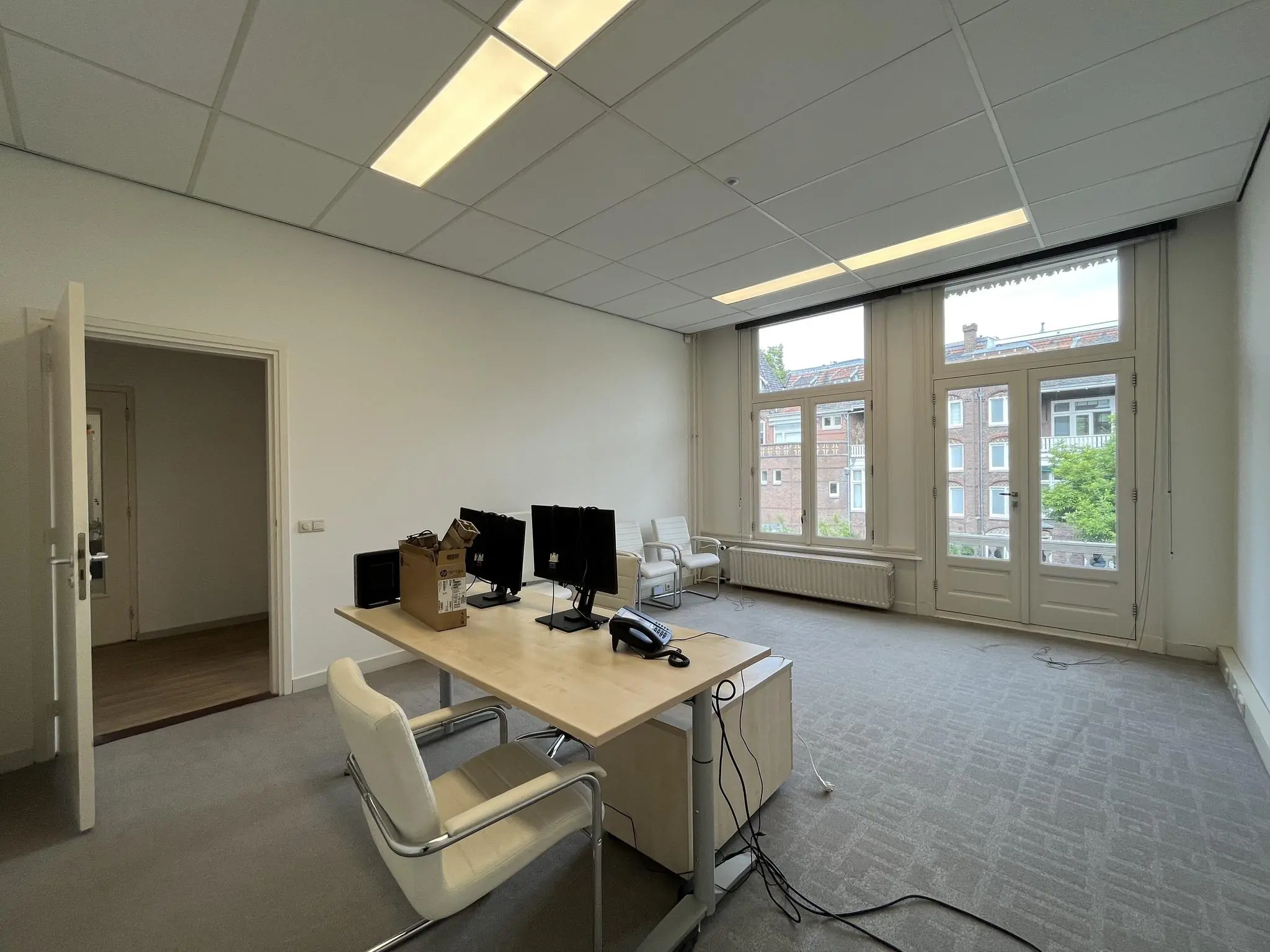 Kantoorruimte aan de Ramstraat met bureau, stoelen, computers en uitzicht op omliggende woongebouwen.