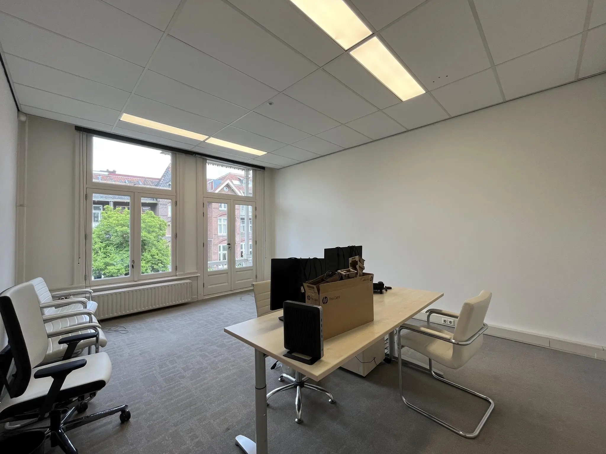 Kantoorruimte aan de Ramstraat met bureaus, stoelen en ingepakte computers bij het raam.