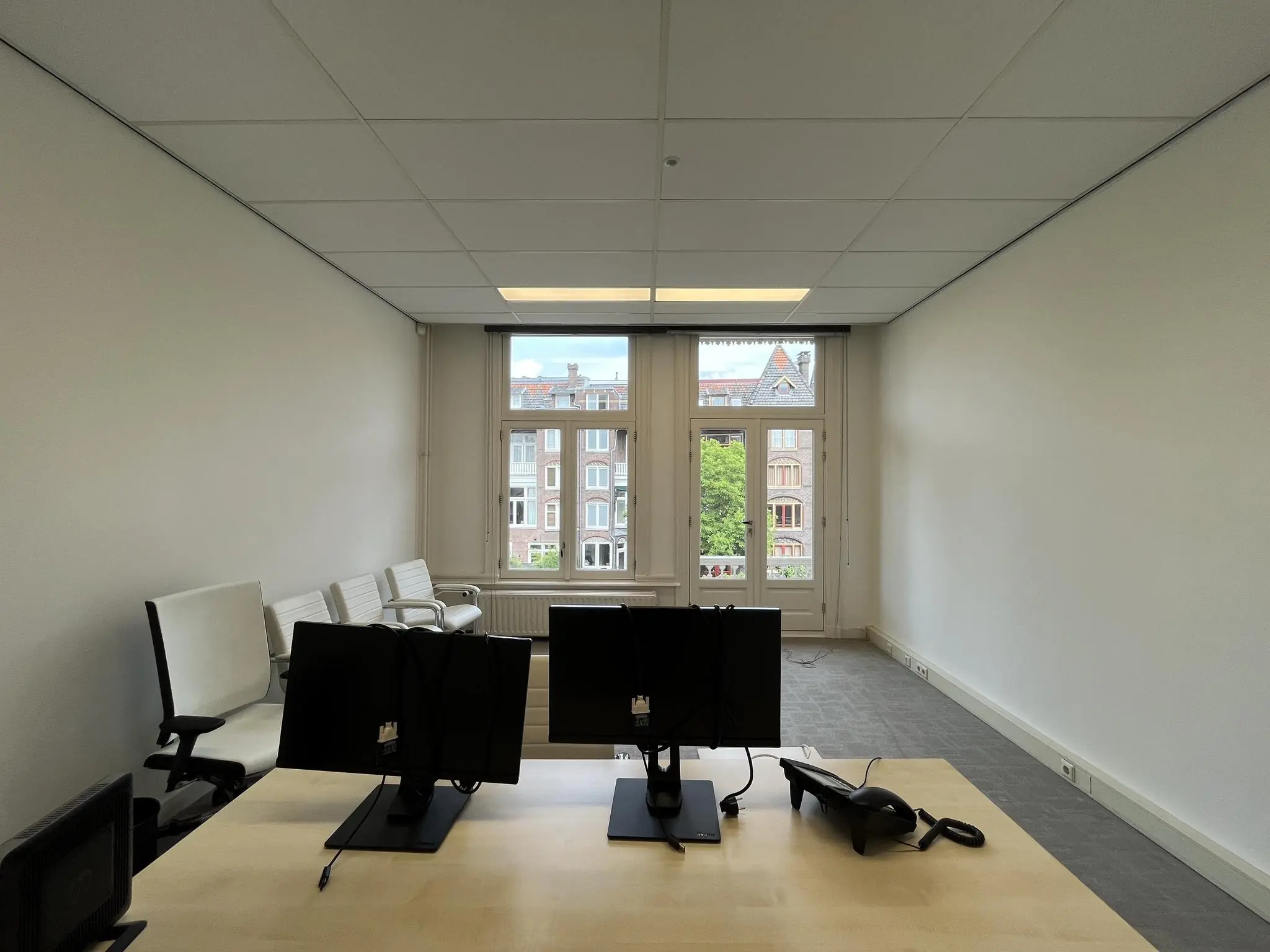 Kantoorruimte aan de Ramstraat met werkplekken, stoelen en uitzicht op klassieke gevels.