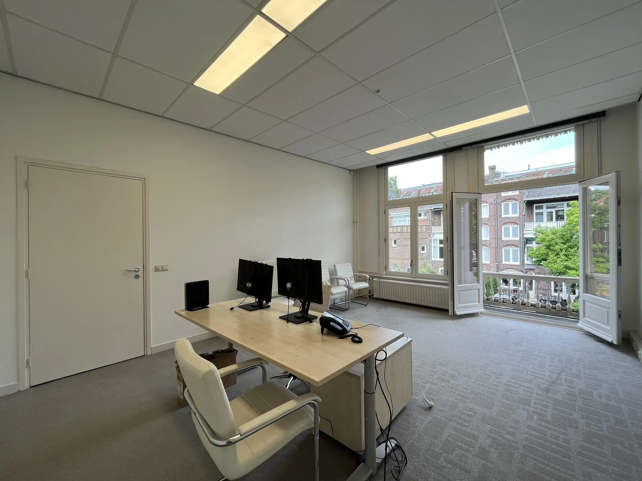 Kantoorruimte aan de Ramstraat met open balkondeuren, twee werkplekken en uitzicht op klassieke stadspanden.