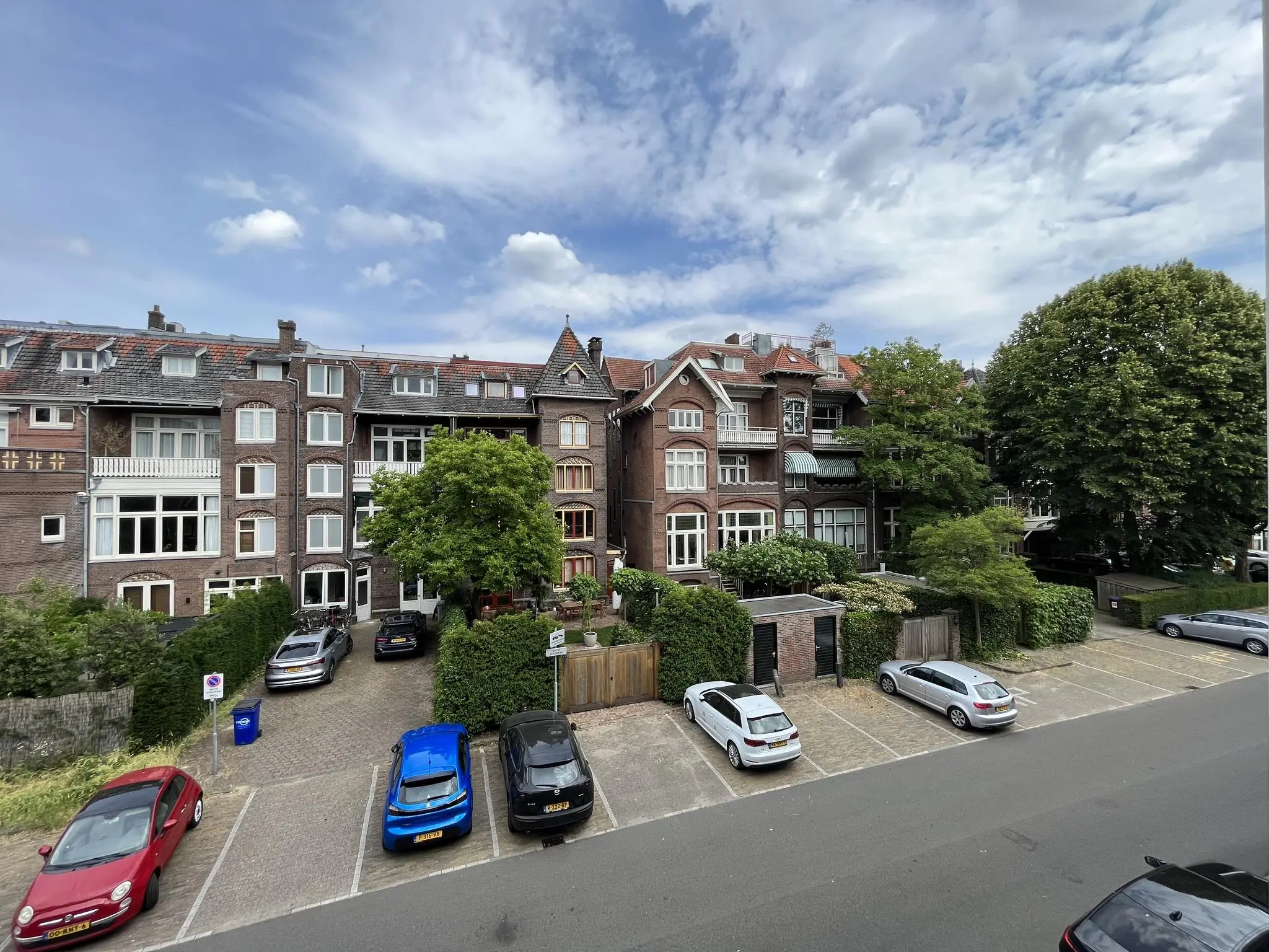 Rij met geparkeerde auto's voor karakteristieke herenhuizen aan de Ramstraat in een groene woonwijk.