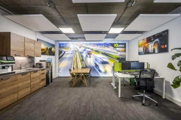 Modern kantoor met keukenhoek, vergadertafel en werkplekken, met een opvallende wanddecoratie van een snelweg en IQ Select-logo.