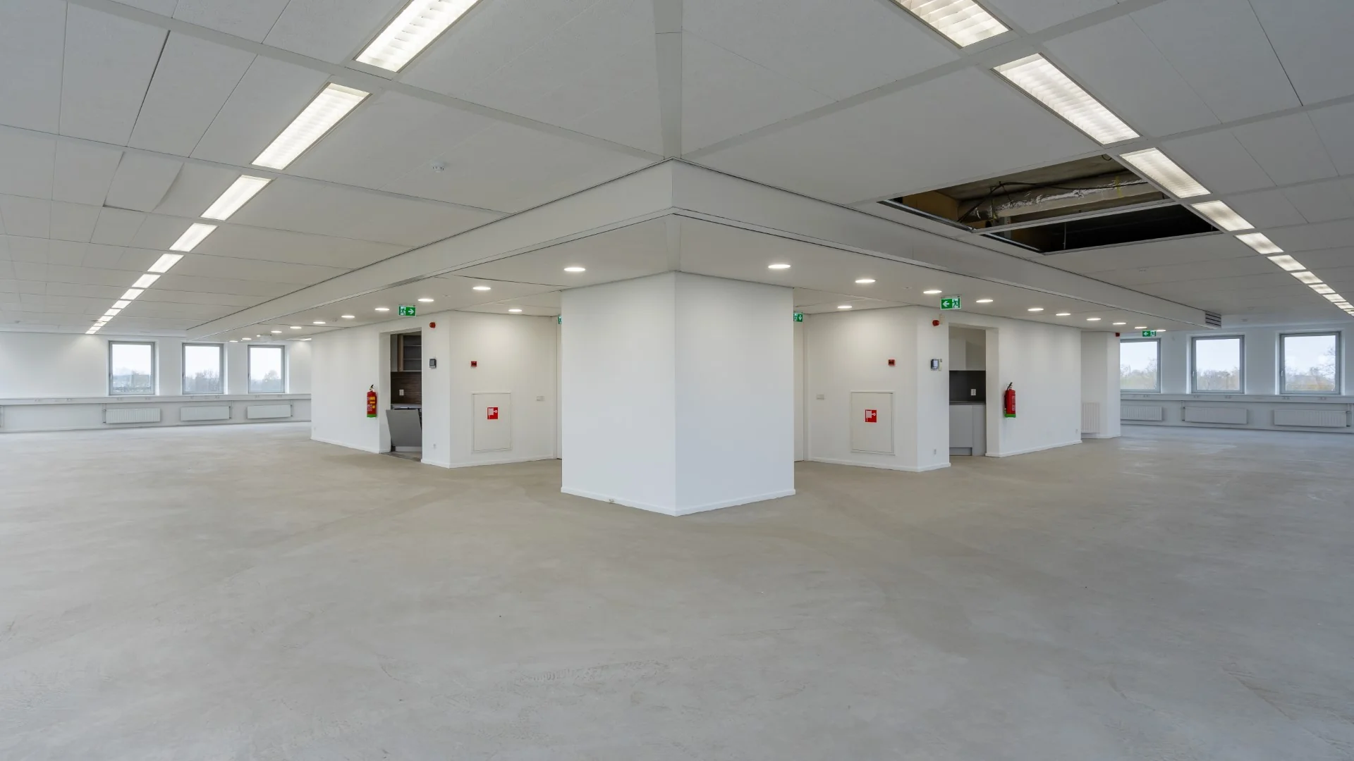 Leeg kantoorpand aan de Printerweg met witte wanden, systeemplafond, grote ramen en betonnen vloer.