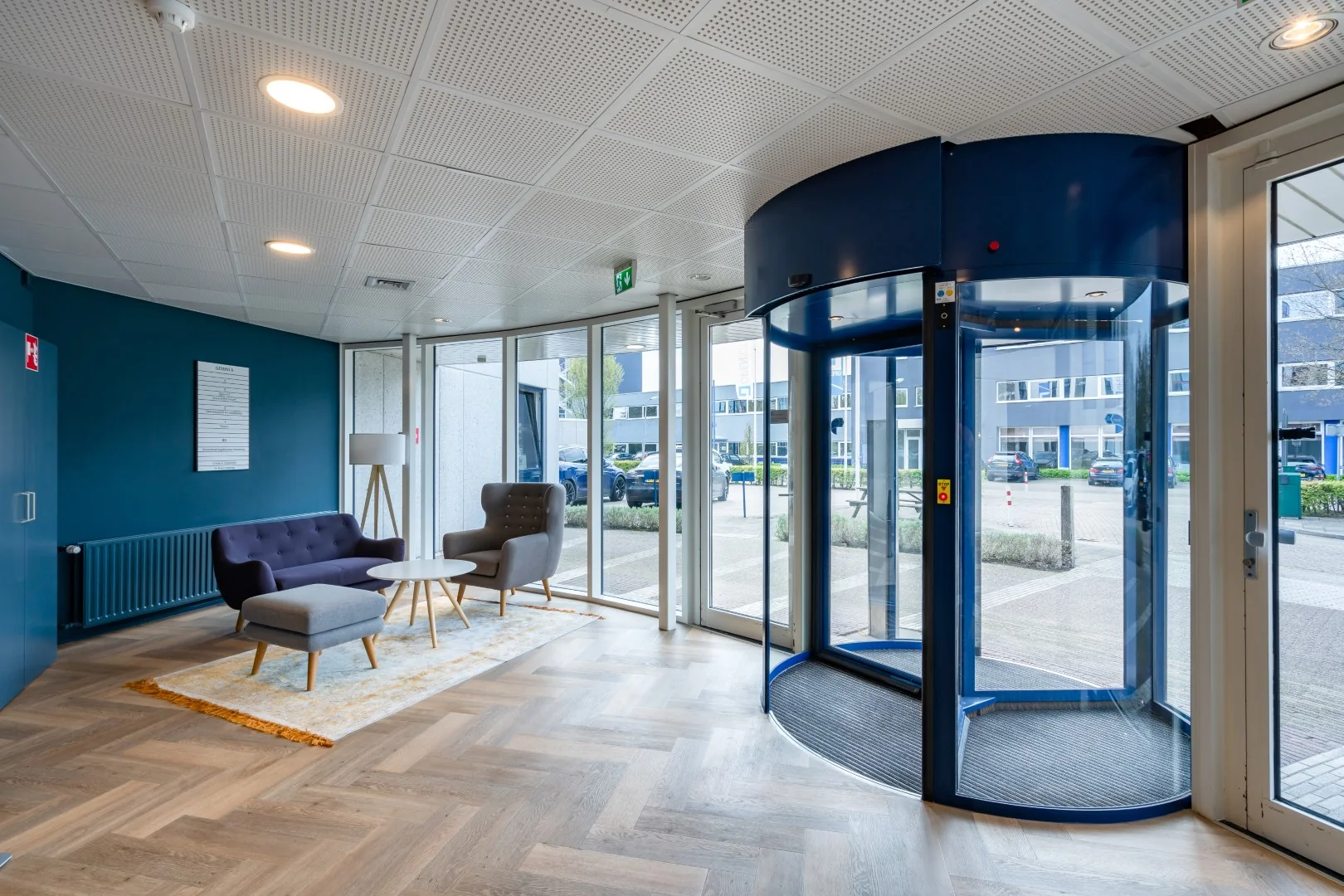 Moderne entreehal van een kantoorpand aan de Printerweg met een draaideur en een wachthoek met zitmeubilair.