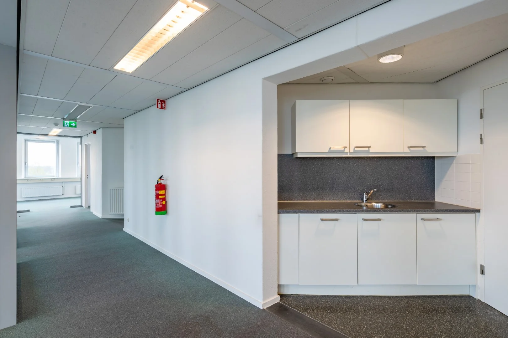 Kleine pantry met witte keukenkastjes en een wastafel in een kantoorruimte aan de Printerweg.