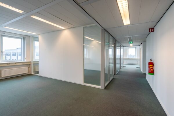 Lichte, lege kantoorruimte aan de Printerweg met glazen wanden en systeemplafond.