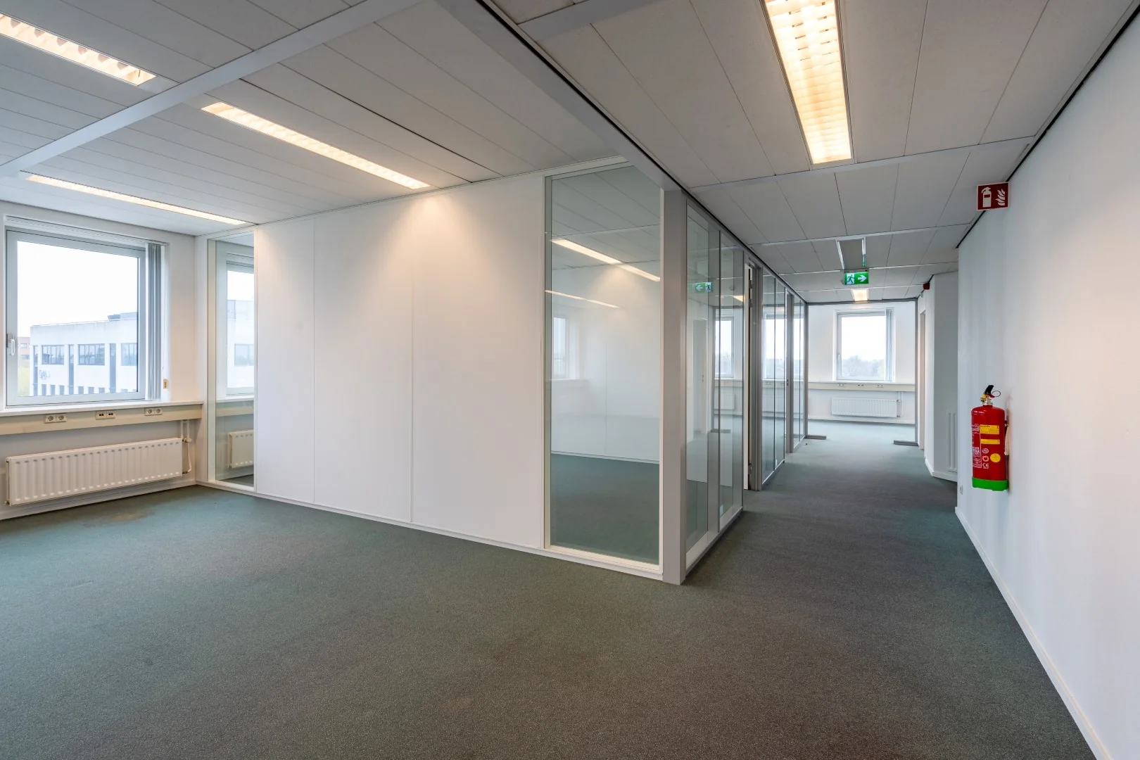 Lichte, lege kantoorruimte aan de Printerweg met glazen wanden en systeemplafond.