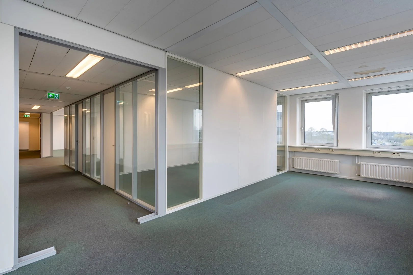 Leeg kantoorpand aan de Printerweg met glazen scheidingswanden en grote ramen.