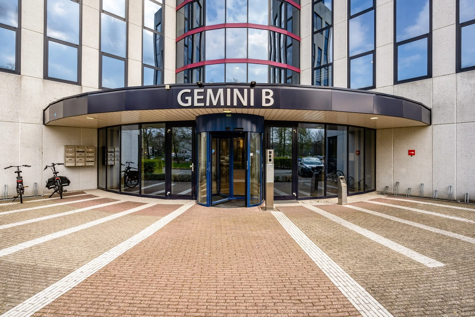 Ingang van kantoorgebouw Gemini B aan de Printerweg met draaideur, fietsenrekken en brievenbussen.