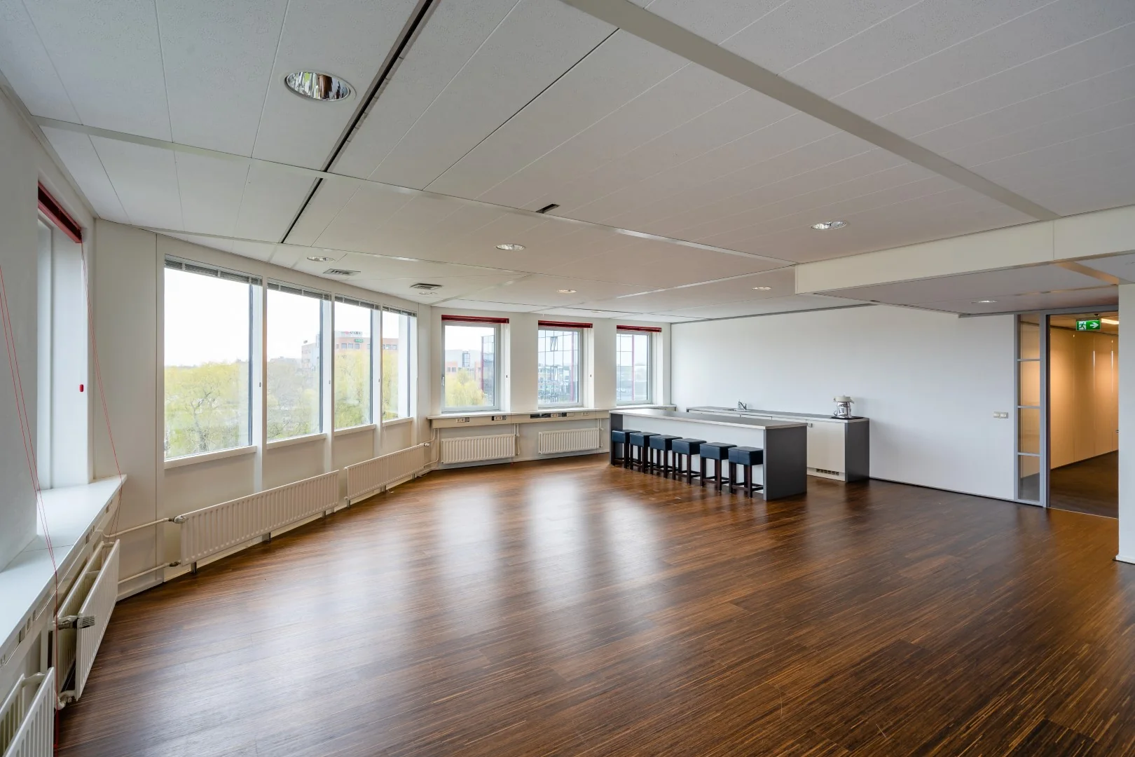 Ruime, lichte kantoorkantine aan de Printerweg met houten vloer, grote ramen en een lange bar met barkrukken.