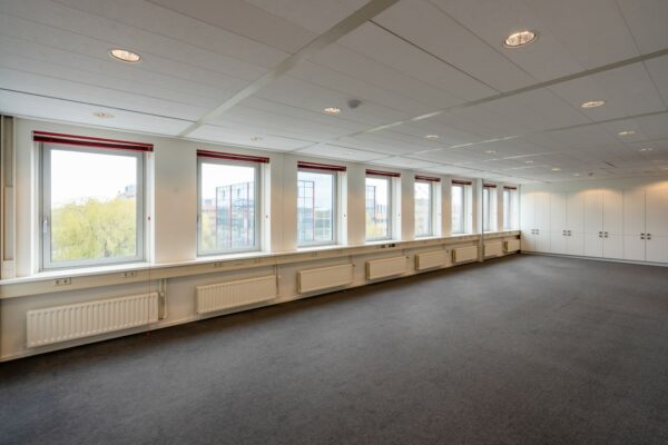 Leeg kantoor met grote ramen, systeemplafond en ingebouwde kasten aan de Printerweg.