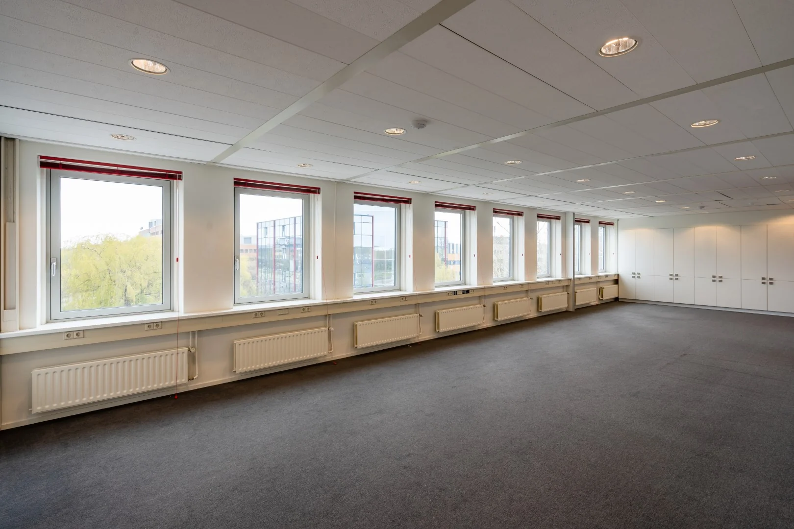 Leeg kantoor met grote ramen, systeemplafond en ingebouwde kasten aan de Printerweg.
