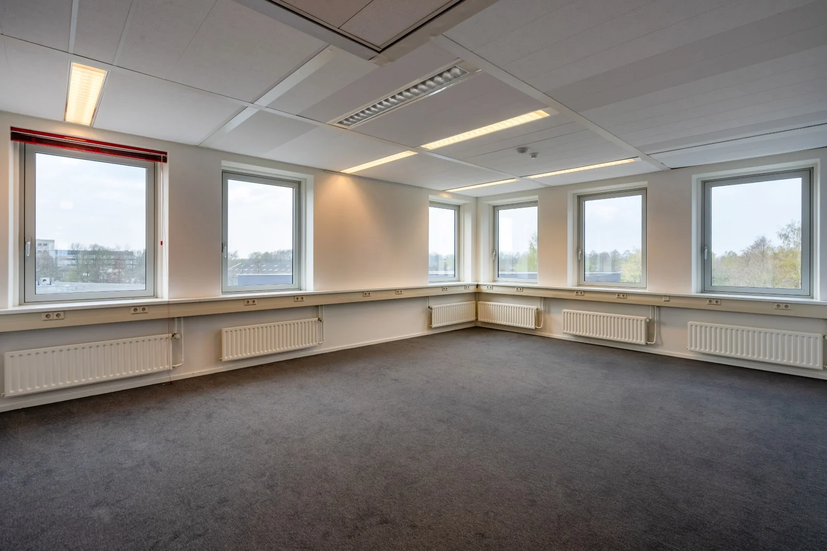 Licht en ruim leeg kantoor op de Printerweg met meerdere ramen en een grijze vloerbedekking.