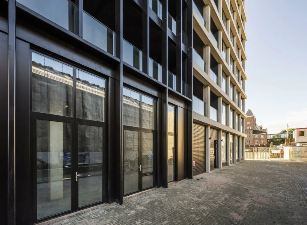 Moderne gevel van een appartementencomplex aan de Oostenburgermiddenstraat in Amsterdam met grote ramen en betonnen balkons.