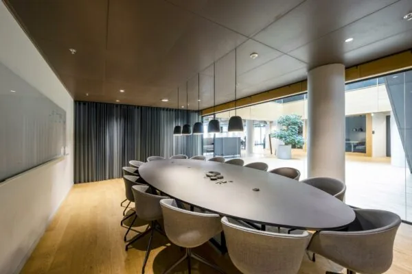 Moderne vergaderruimte aan het Rokin met een ovale tafel, grijze stoelen, hanglampen en glazen wanden.