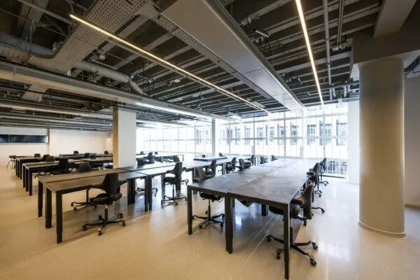 Ruim, modern ingericht kantoor of studiegebied aan het Rokin met grote bureaus, ergonomische stoelen en veel natuurlijk licht.