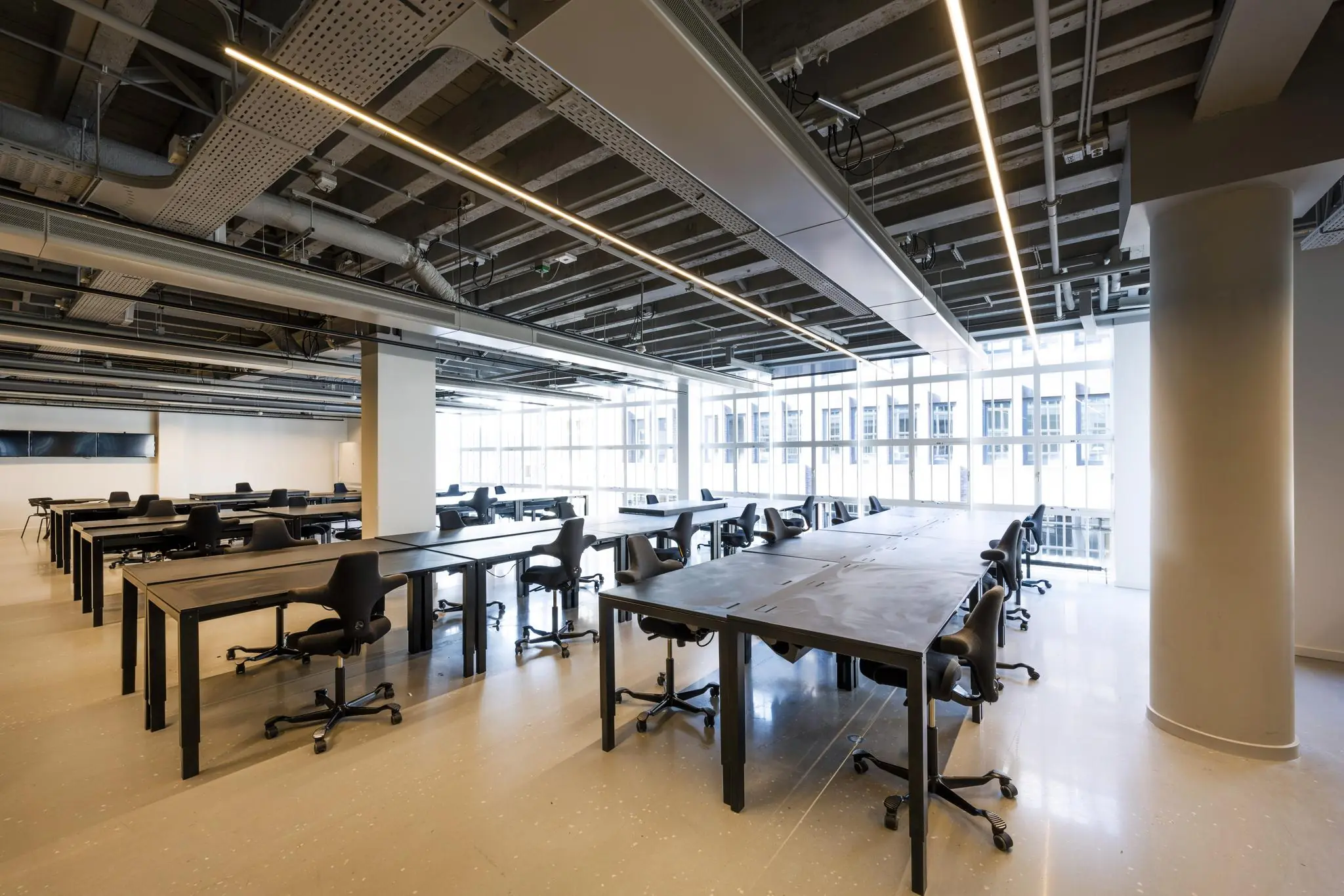 Ruim, modern ingericht kantoor of studiegebied aan het Rokin met grote bureaus, ergonomische stoelen en veel natuurlijk licht.