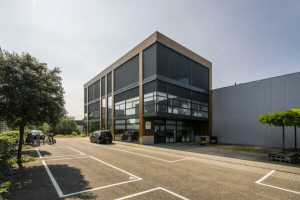 Modern kantoorgebouw aan de Asterweg met grote ramen en een deels lege parkeerplaats op de voorgrond.